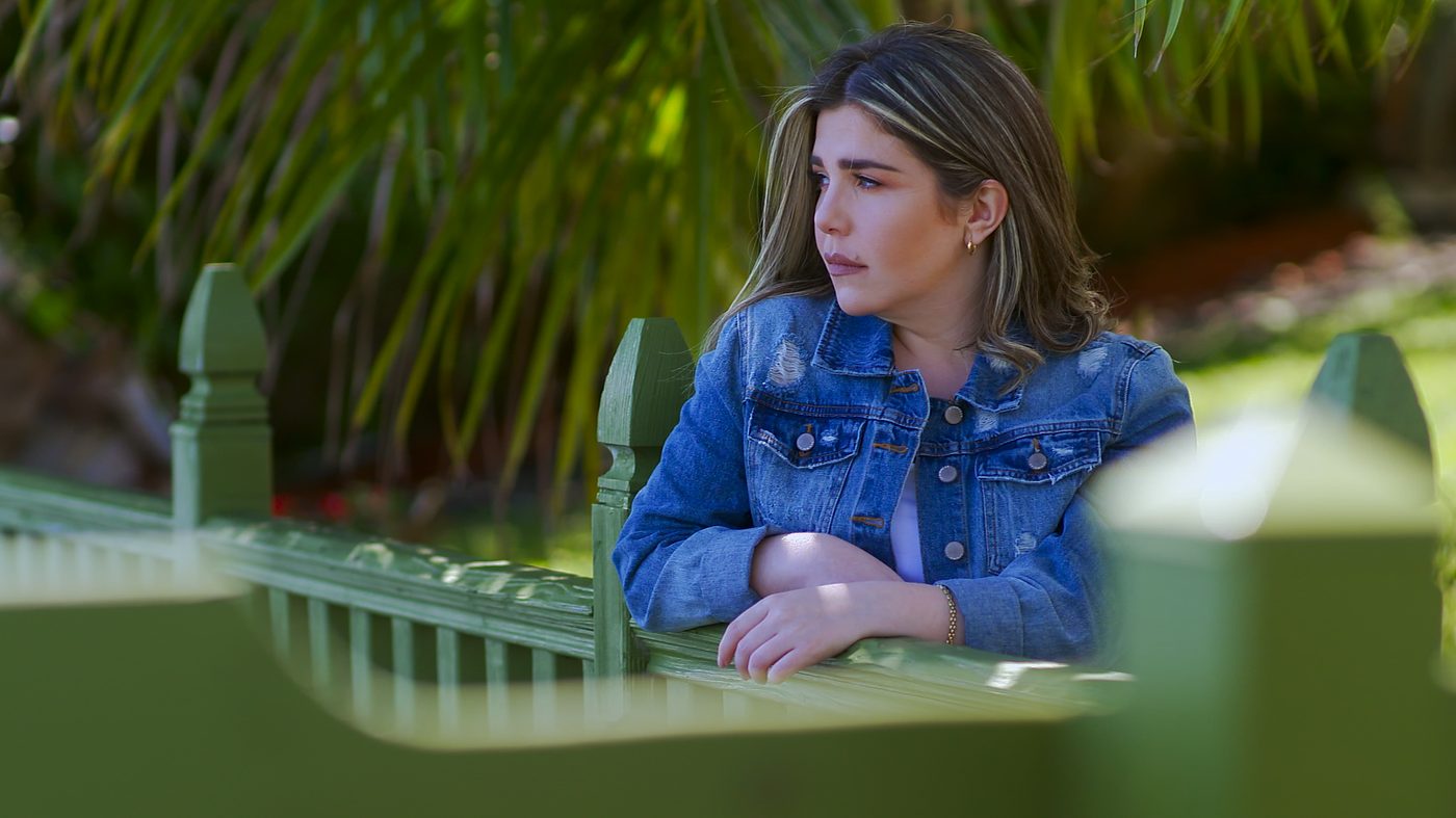 Elizabeth Sanchez con chaqueta de mezclilla, mirando pensativa en un jardín